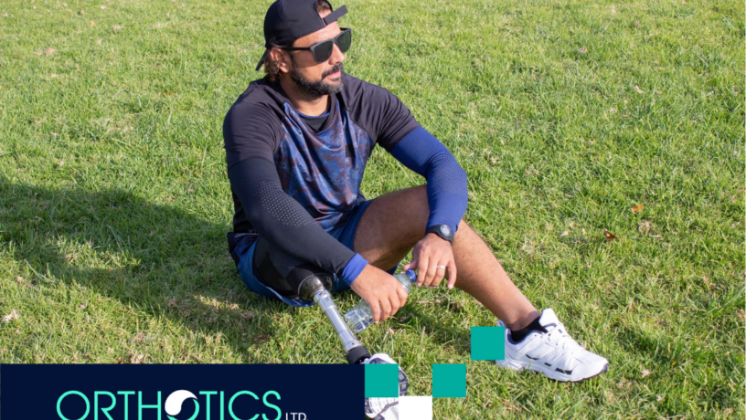 An amputee wearing prosthetics sitting on a grass ooutdoors