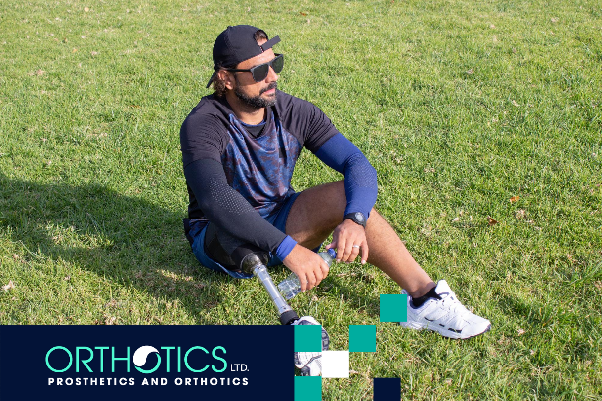 An amputee wearing prosthetics sitting on a grass ooutdoors